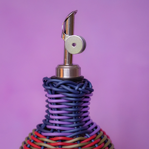Decorative bottle with woven design and metallic nozzle on a purple background