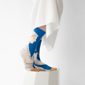 Woman in white dress wearing Statue Bonne Maison socks on white backdrop.