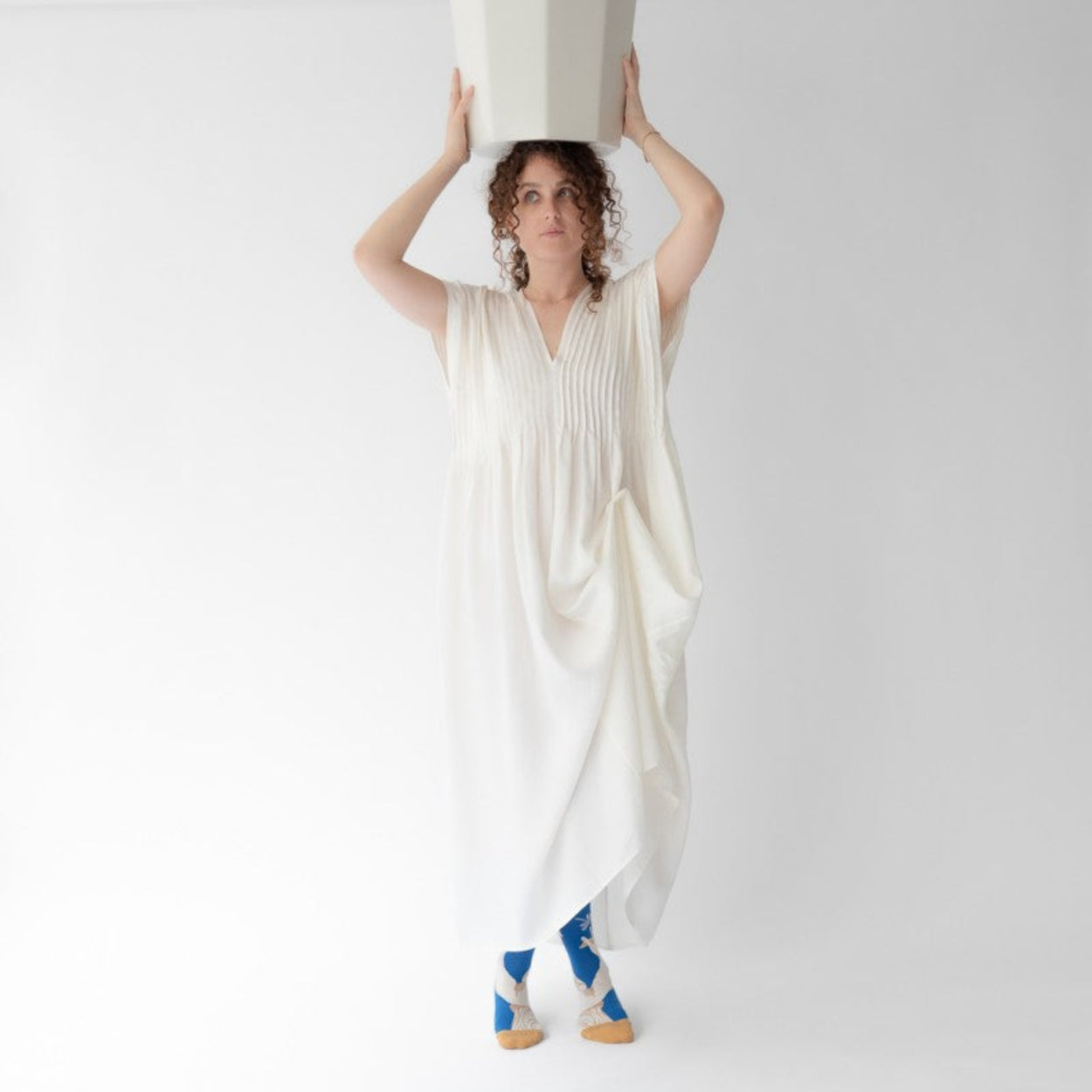 Woman in white dress wearing Statue Bonne Maison socks on white backdrop.