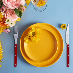Sabre Paris Burgundy cutlery with yellow plates and flowers on blue tabletop