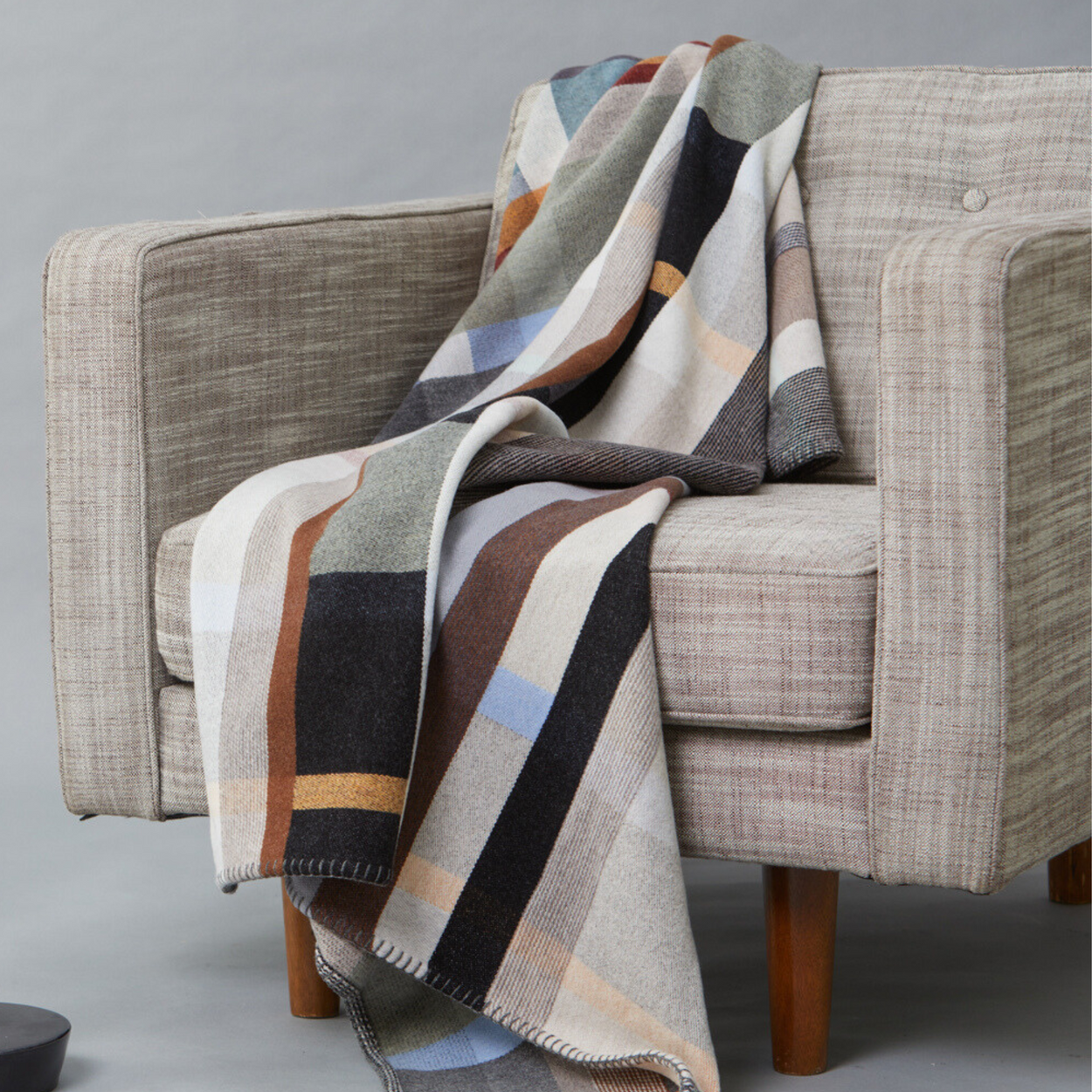 Wallace Sewell Premium Chipperfield  Merino lambswool throw in pale brown tones, draped on arm chair.