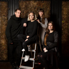 Four Fischersund family posing in a dark room with a textured wall.