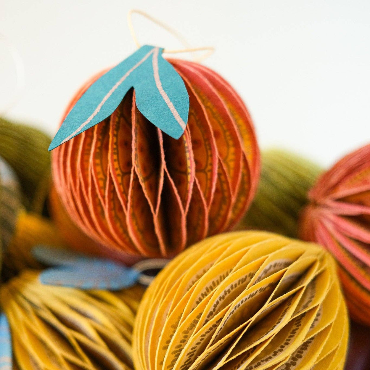 Decorative paper balls in orange and yellow with leaf accents in a bowl.