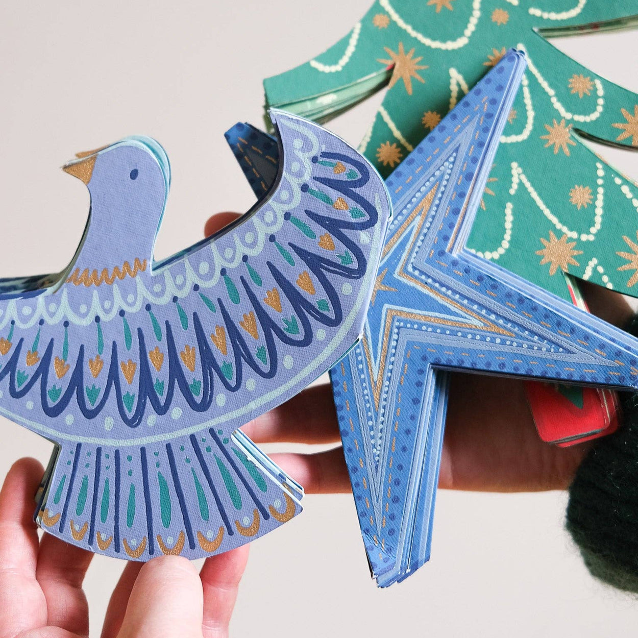 Colorful paper craft shapes, including a bird and star, held by a hand against a neutral background.