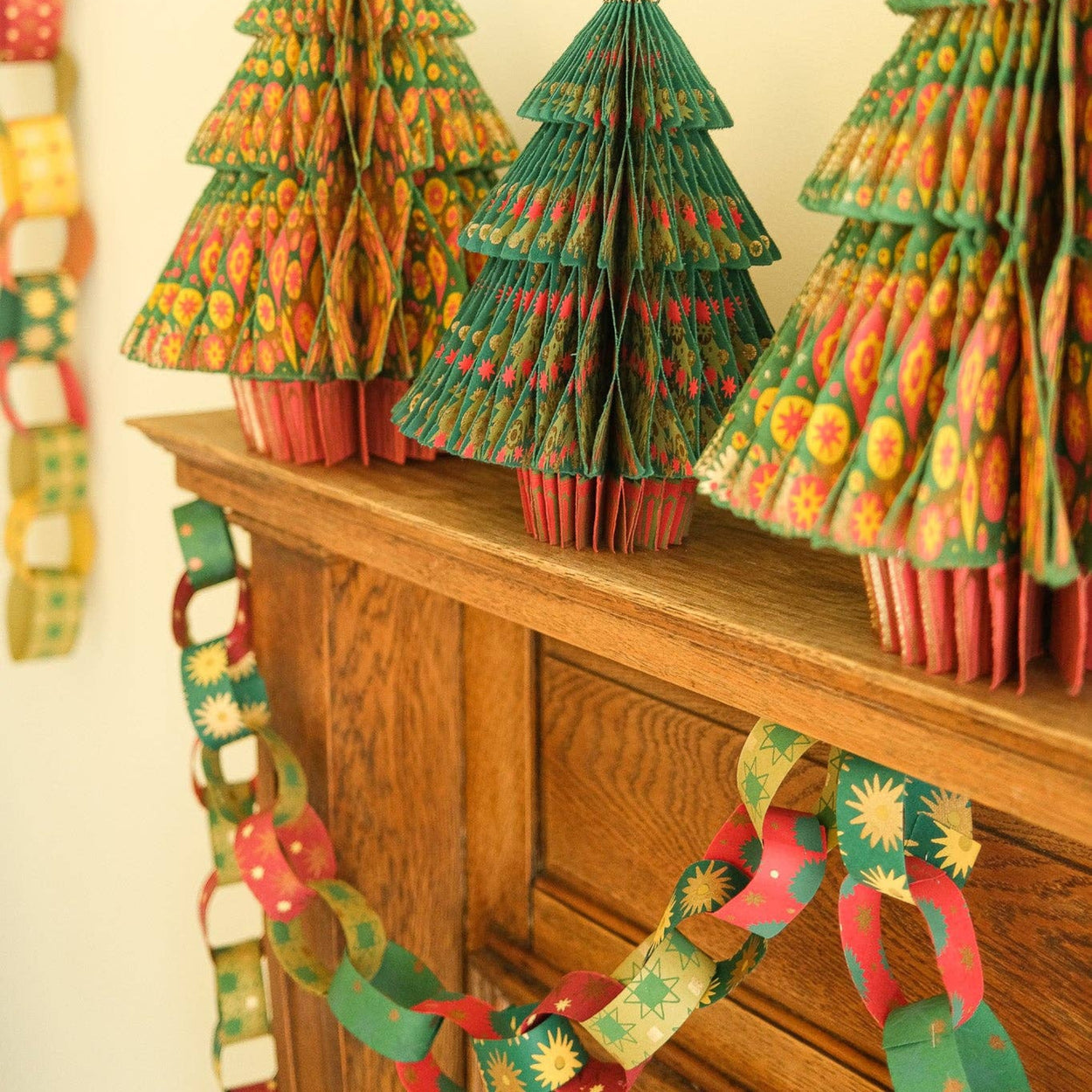 Decorative paper Christmas trees on a wooden surface with festive garlands.