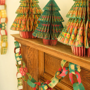 Decorative paper Christmas trees on a wooden surface with festive garlands.