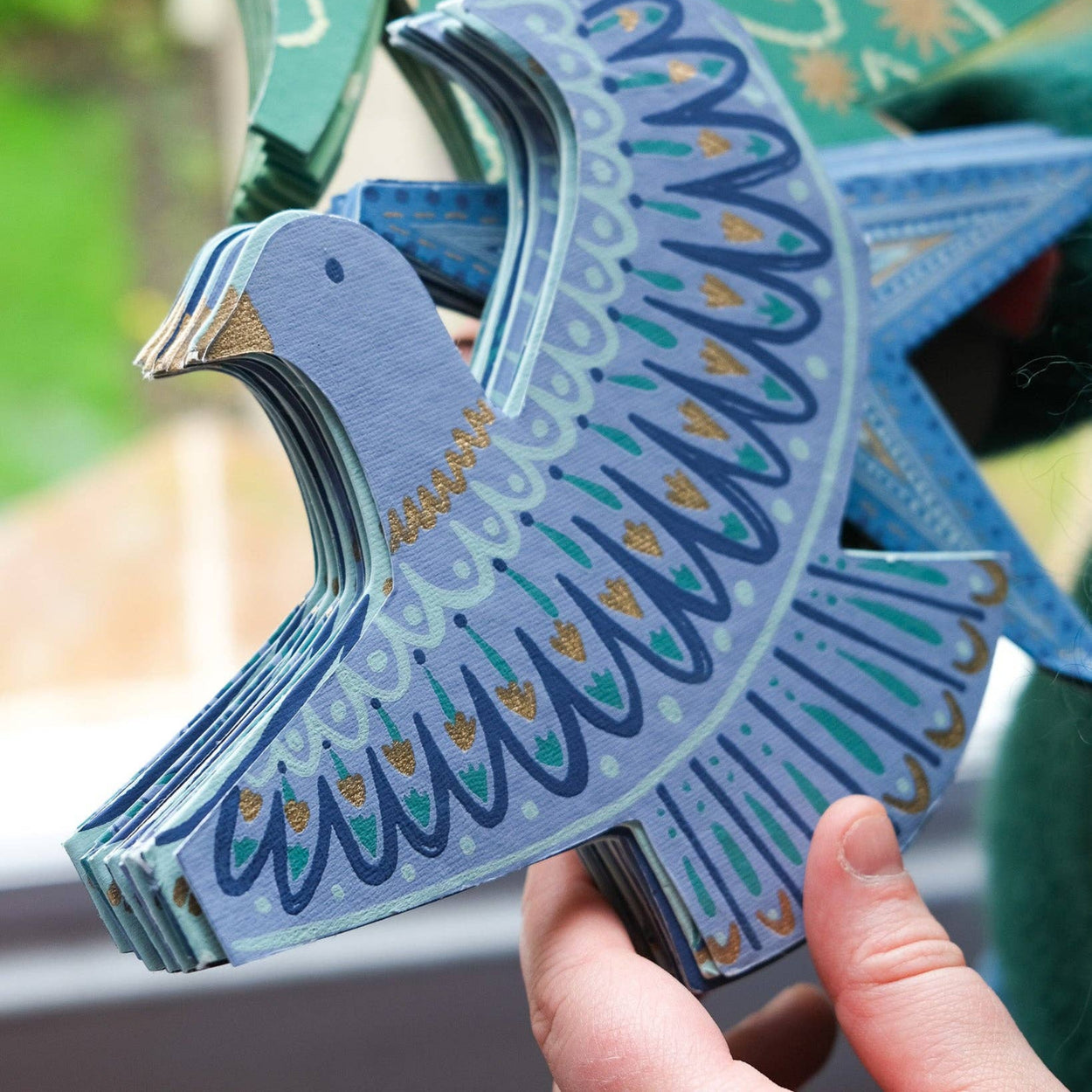 Decorative blue and green paper garland held by a hand with a blurred natural background
