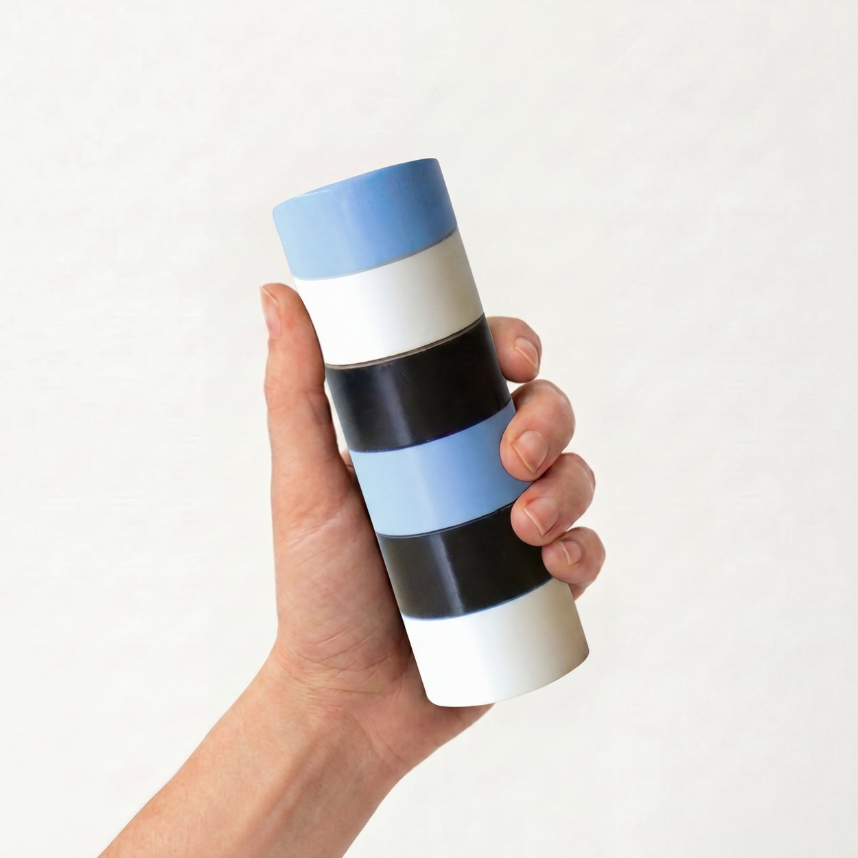 Hand holding a cylindrical Semi D salt and Pepper grinder with blue, white, and black stripes on a white background