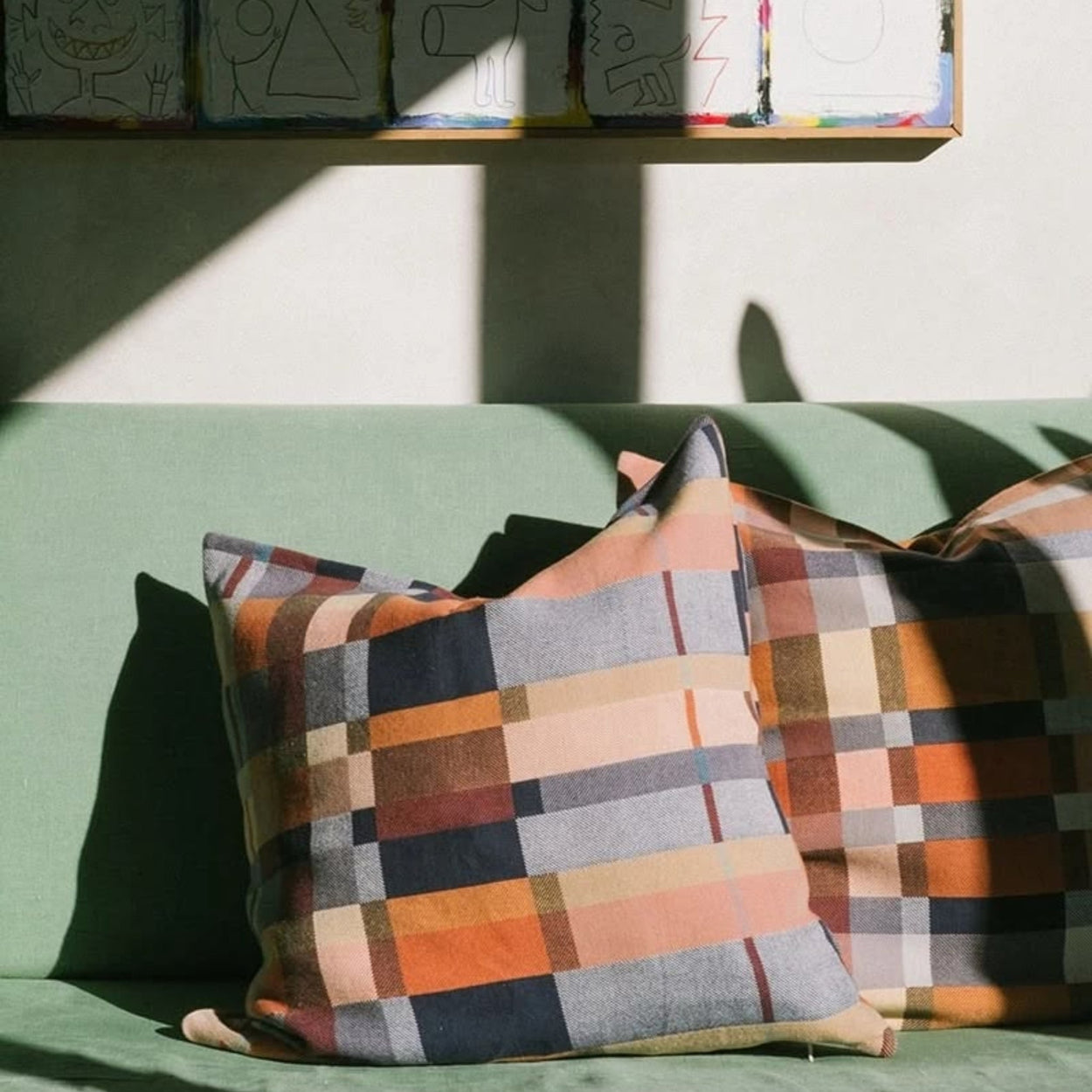 Mungo Karoo Colourful double cotton checkered pillows on a green couch with a wall of colourful artwork in the background.