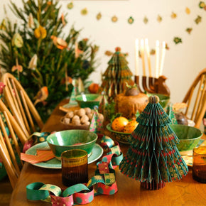 Decorated dining table with Christmas trees, candles, and a tree-shaped paper chain.