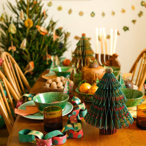 Decorated dining table with Christmas trees, candles, and a tree-shaped paper chain.