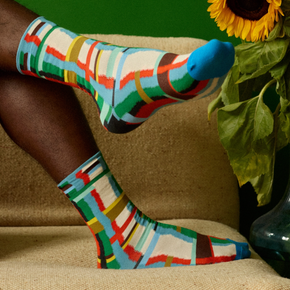 Man wearing Bonne Maison Blue Grid socks on beige couch with sunflower.