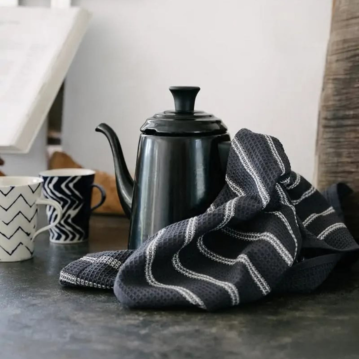 Black teapot and patterned black and white towel on a kitchen counter.