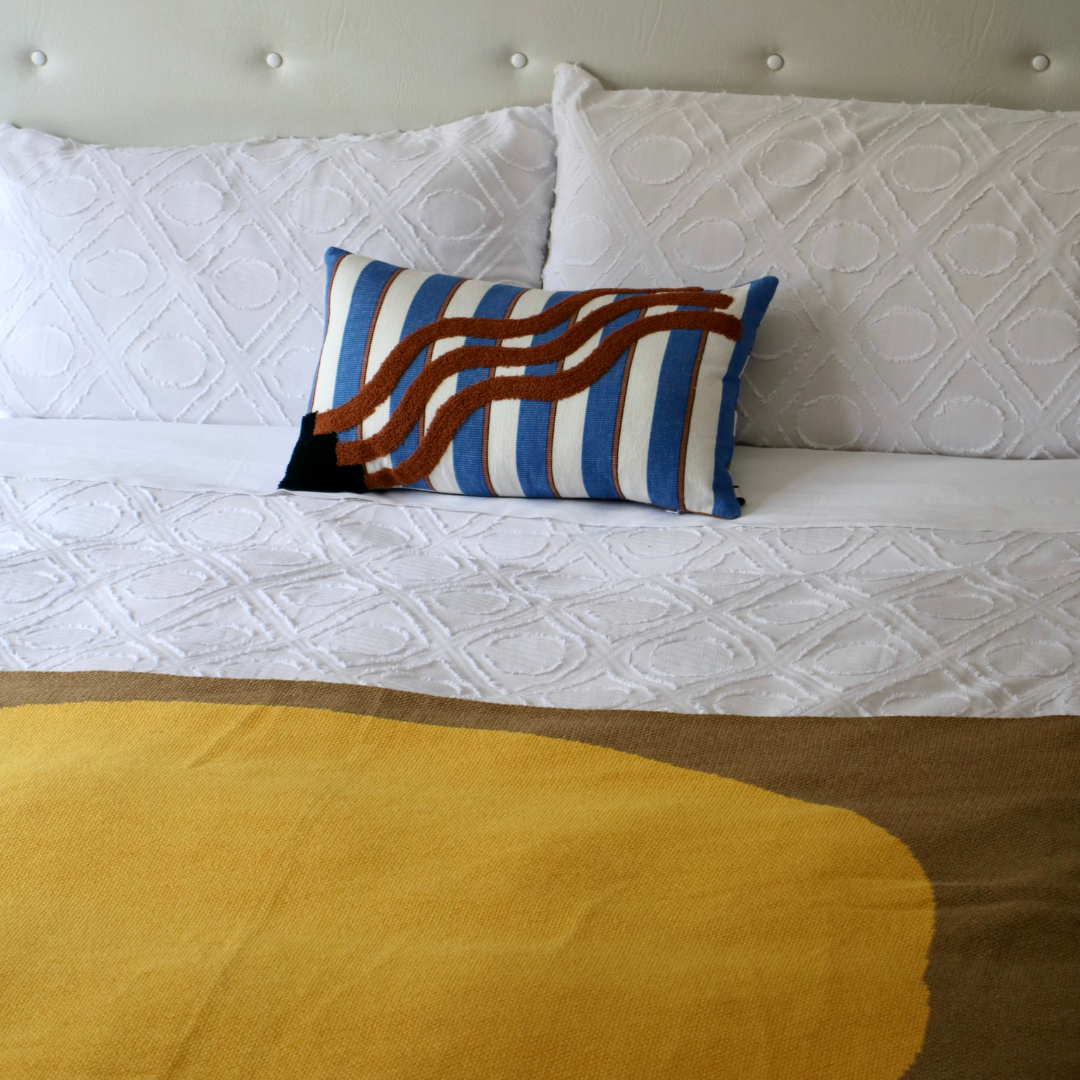 Striped embroidered Cushion Cover in brown with yellow blanket on white bed.