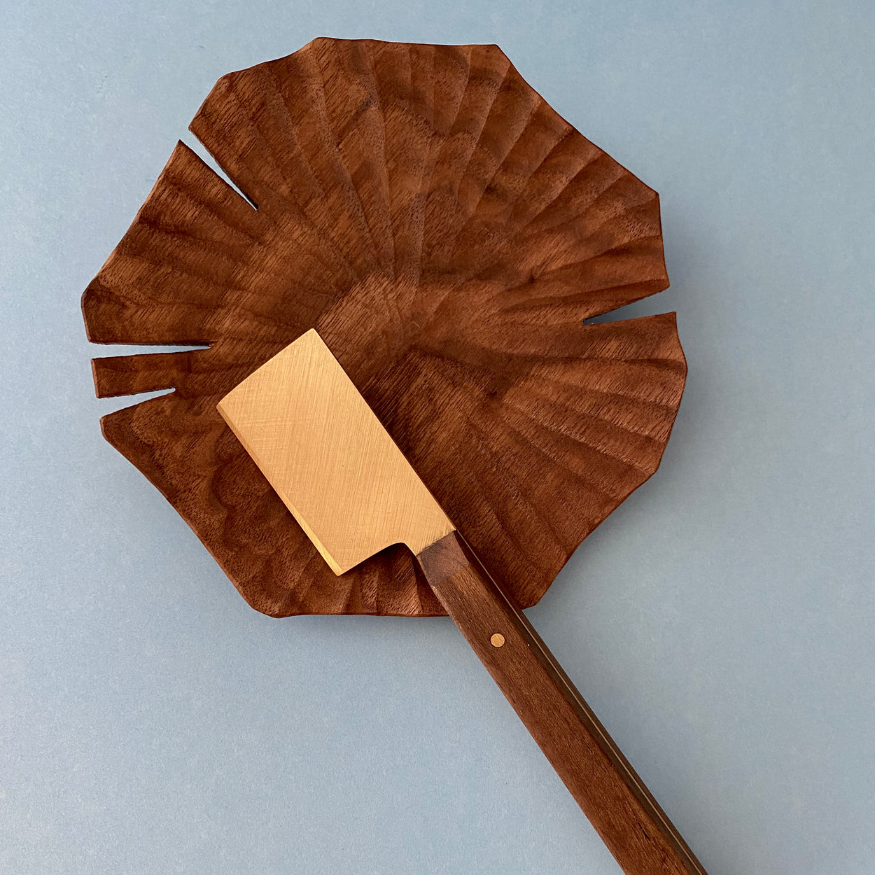 Handmade Walnut & Brass cheese knife against blue background with Lotus leaf carved wood plate