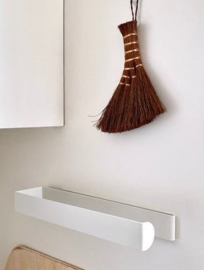 Paper Towel Roll Holder -  White mounted on wall horizontally with wood chopping boards and kitchen brush hanging above it.