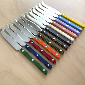 Sabre Bistrot Cheese Knife in 12 colours on pale wood tabletop.