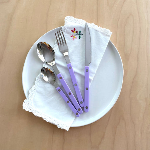 Sabre Bistrot Paris 4 piece cutlery set in Lilac on white plate with vintage napkin on pale wood table.