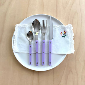 Sabre Bistrot Paris 4 piece cutlery set in Lilac on white plate with vintage napkin on pale wood table.