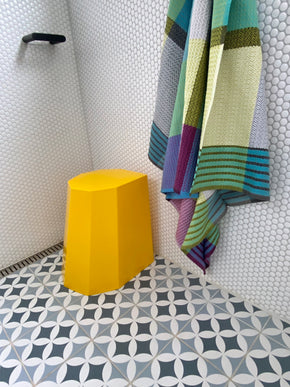 Arnold Circus Stool in yellow in tiled pale grey shower recess with bright towels.