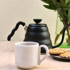 Handmade Ceramic Coffee Mug - Large by Richard Beauchamp on pale wood background with yellow flowers, cookies and black teapot..