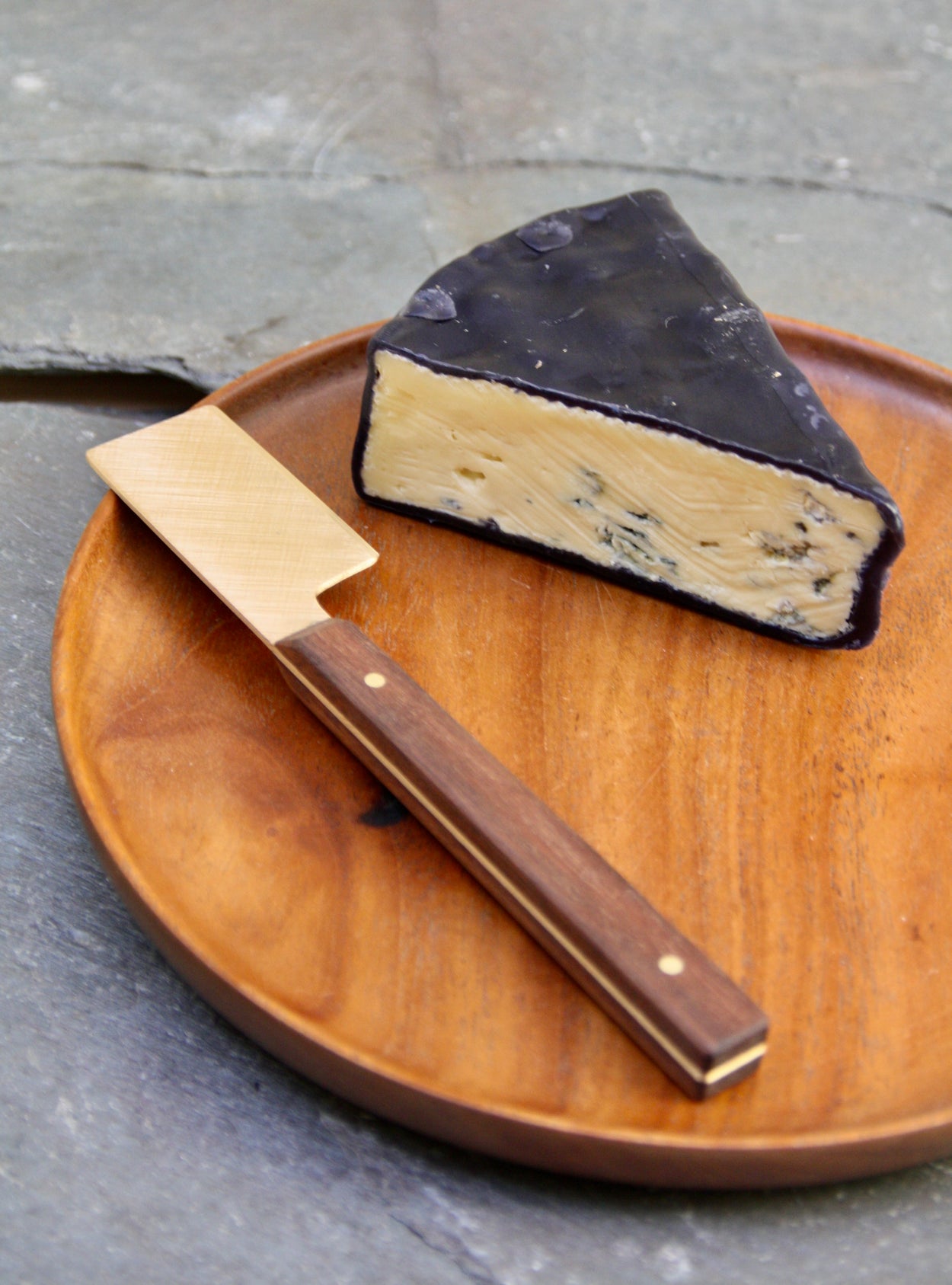 Handmade Walnut & Brass cheese knife against blue background with blue cheese and wood plate