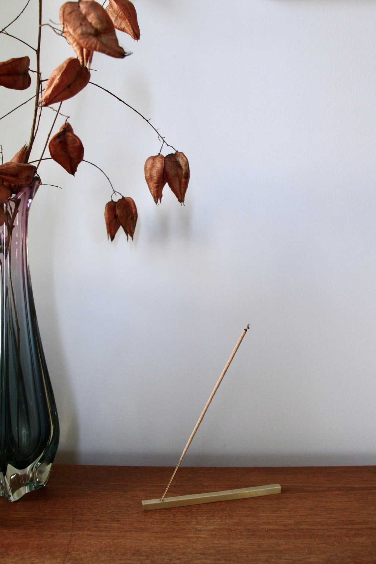 Juniper Ridge Campfire Incense - Desert Pinon, burning in incense holder on wood shelf with vase and flowers.