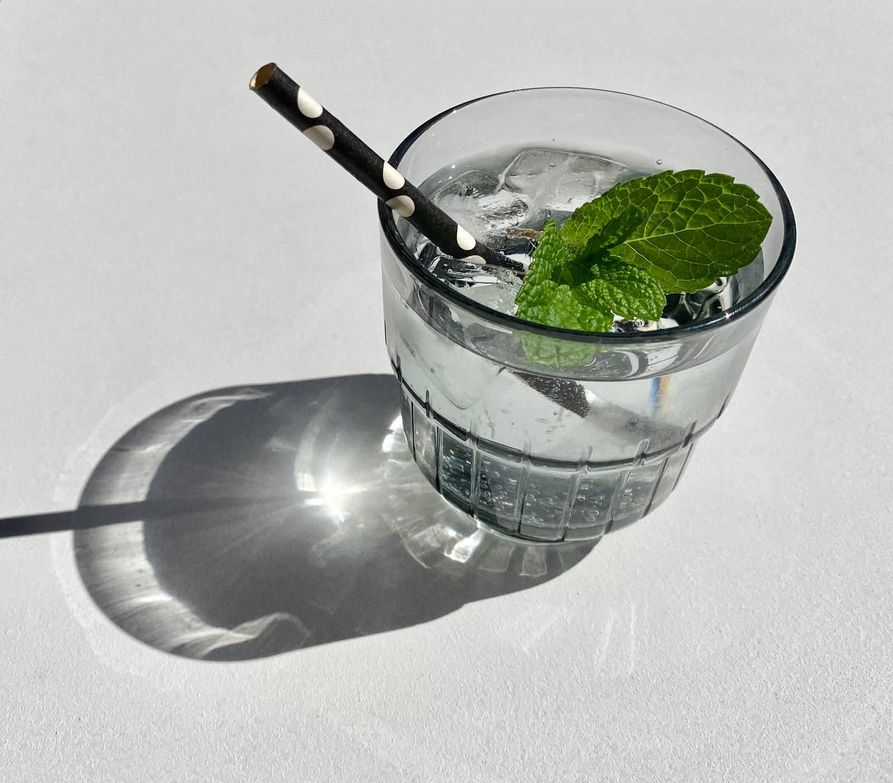 Smokey Grey Portuguese glass with polka dot straw and mint leaf in water with white background.