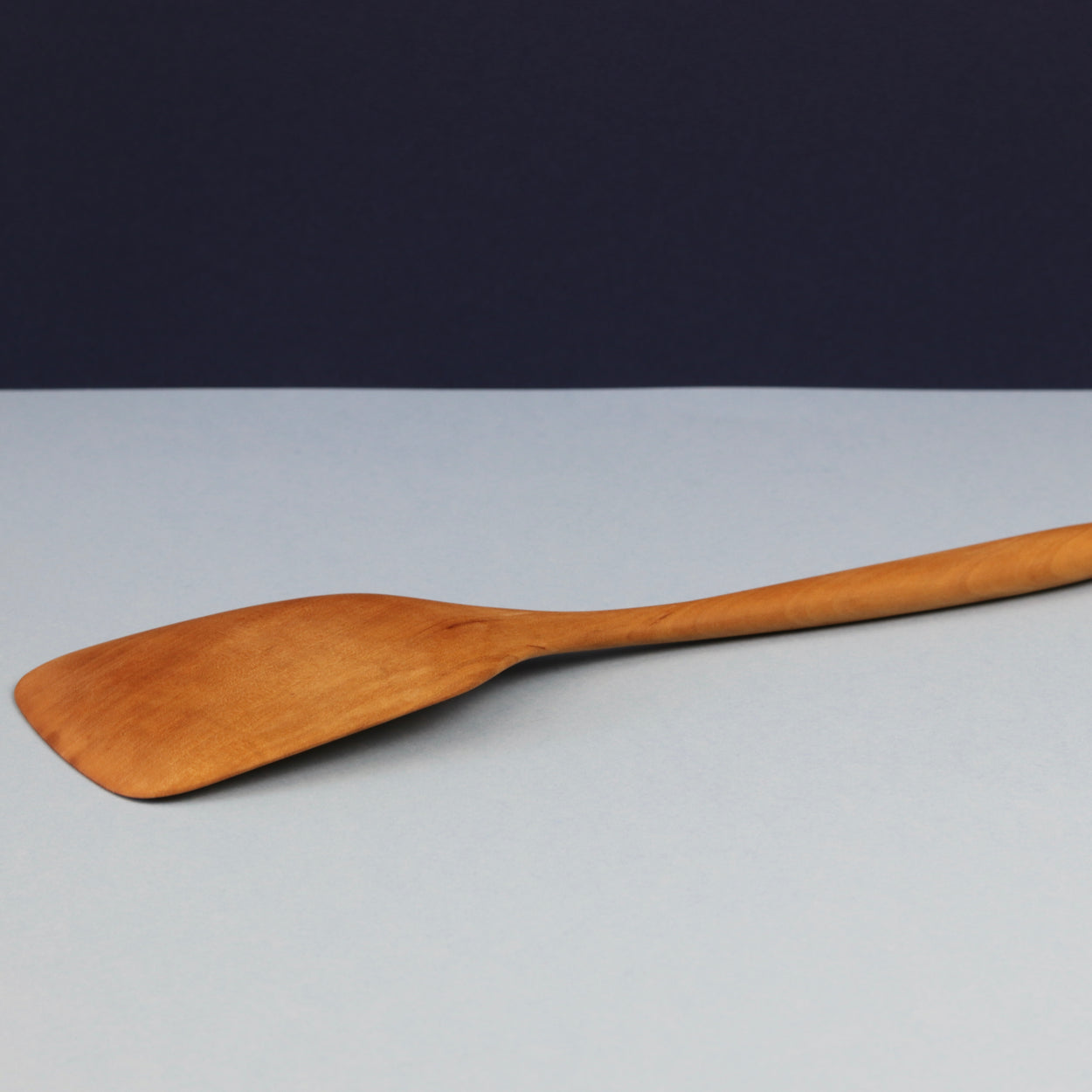 Handmade Pear Wood Kitchen Spatula, lying face down against blue background