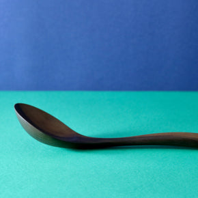 Side view of Handmade Walnut Wood Soup Ladle with green and blue background by Civil Dawn Studio