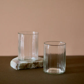Hand crafted recycled glass tumblers x 2, one on a slab of marble against a pink and brown background.