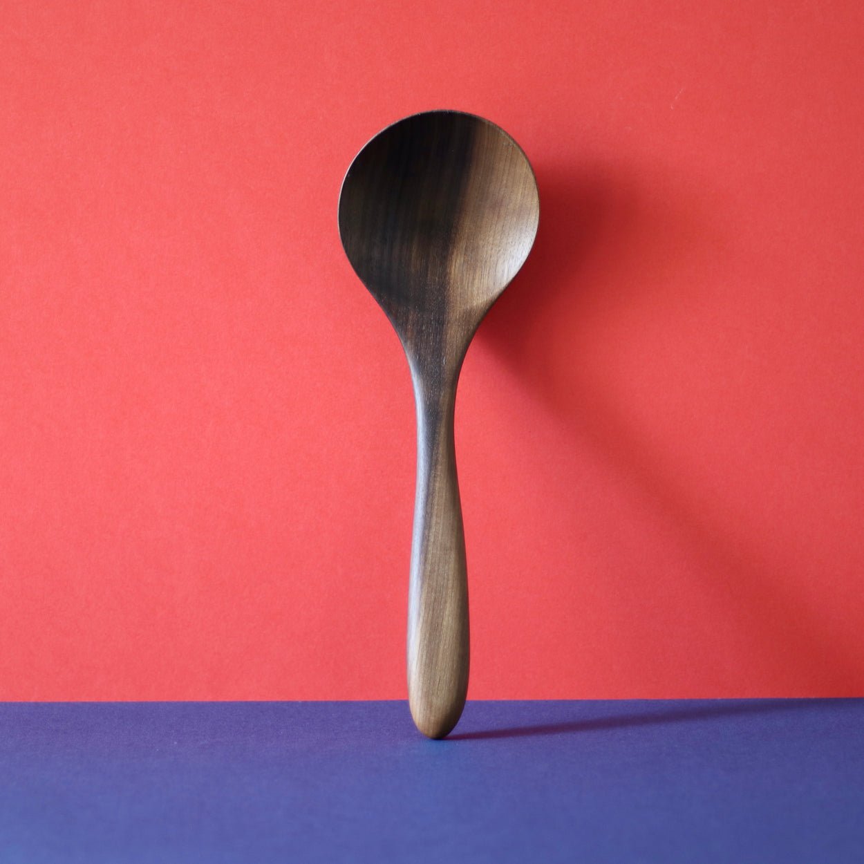 Upright Handmade Walnut Wood Soup Ladle with red and blue background