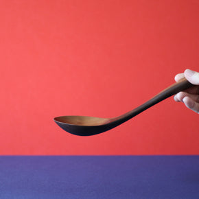 Side view of hand holding a Handmade Walnut Wood Soup Ladle with red and blue background by Civil Dawn Studio
