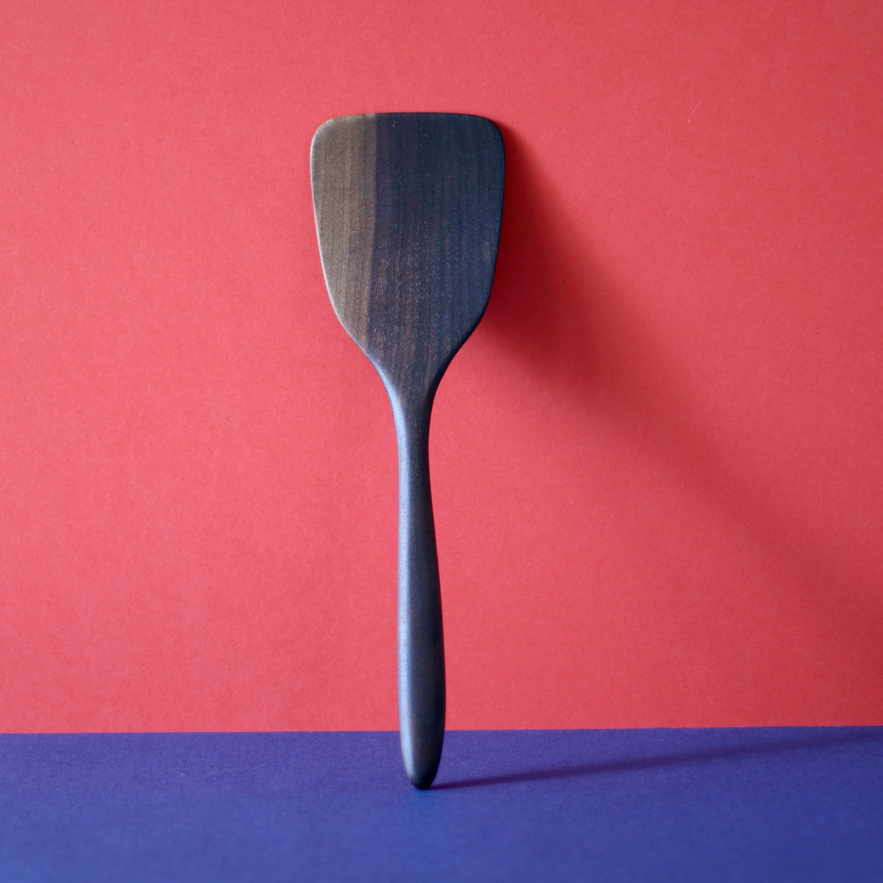 Handmade Walnut Wood Spatula upright with red and blue background. By Civil Dawn Studio.