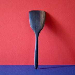 Back view of Handmade Walnut Wood Spatula upright with red and blue background. By Civil Dawn Studio.