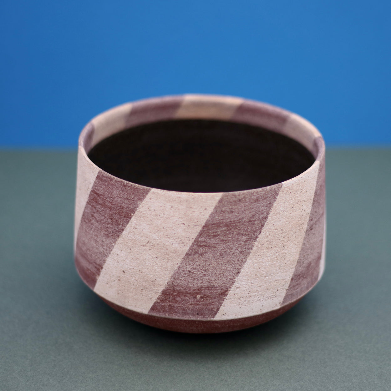 Ceramic Medium Stripe Bowl by Amanda-Sue Rope with blue green background. Top angle view.