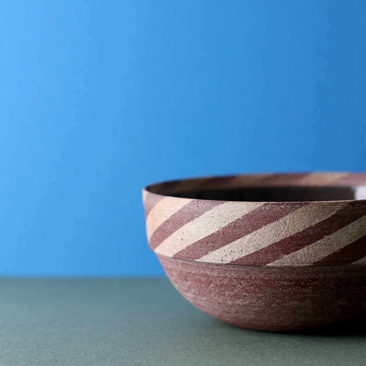 Ceramic Thin Stripe Bowl by Amanda-Sue Rope with blue green background. Close up view.