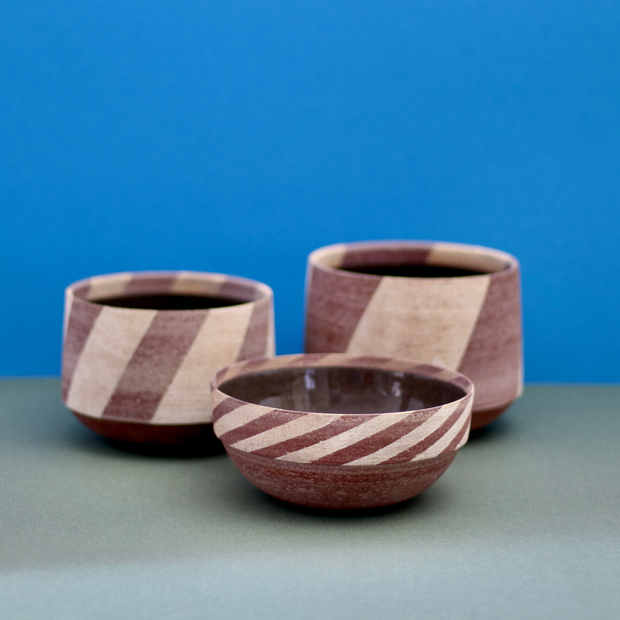 Group of three Ceramic Stripe Bowls by Amanda-Sue Rope with blue green background.