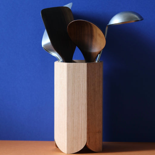 Handmade Wood Kitchen Utensil Holder in oak against a blue and brown background with various utensils inside it.