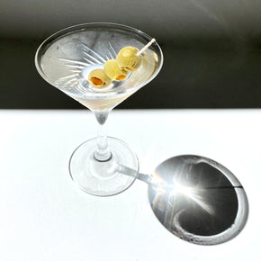 Japanese martini glass with 3 olives and liquid, against white and shadow backdrop