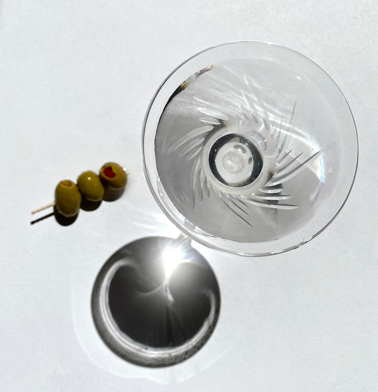 Viewed from above, Japanese martini glass, with olives on pick lying on it's side, against white backdrop