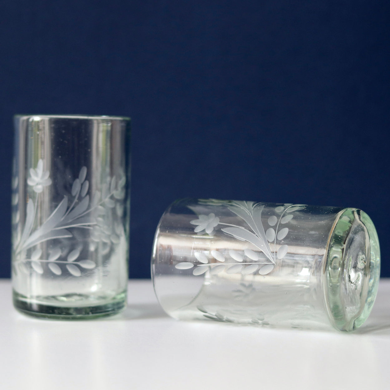 Hand blown etched glass tumbler with blue and white background. One upright ,one lying on it's side.