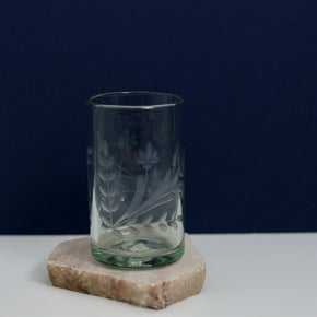 Hand blown etched glass tumbler with blue and white background on marble block.