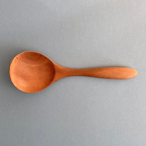Handmade Pear Wood Soup Ladle lying against blue background.