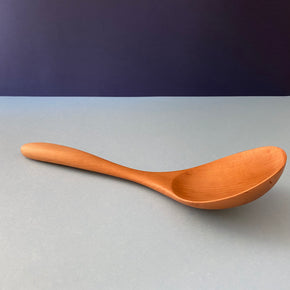 Handmade Pear Wood Soup Ladle lying against blue background