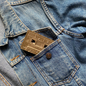 Bronze Cassette Mix Tape by Nancy Pearce half poking out of a denim jacket breast pocket