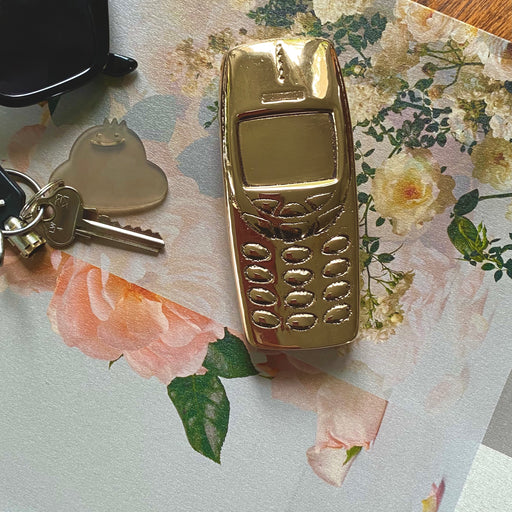 Bronze Nokia phone by Nancy Pearce sitting on book with roses with keys and sunglasses.