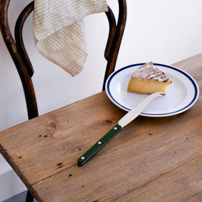 Sabre Bistrot Cheese Knife in Green on vintage wood table with vintage plate, chair and cheese wedge.
