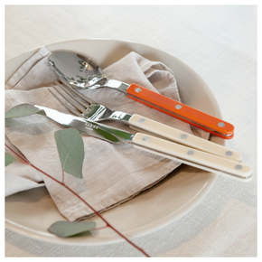 Sabre Paris Bistrot Ivory cutlery with orange spoon on linen napkin on neutral plate.