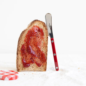 Sabre Paris Bistrot Butter Spreader in Burgundy leaning against a slice of toast with strawberry jam spread on it.
